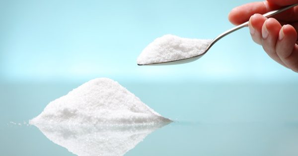 A pile of salt and a hand holding a silver spoon