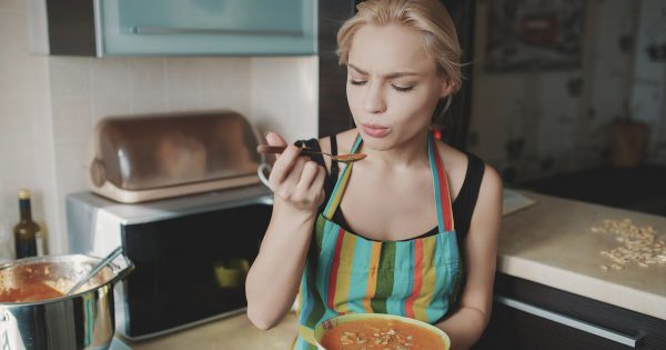 Young woman enjoying pumpkin soup in kitchen