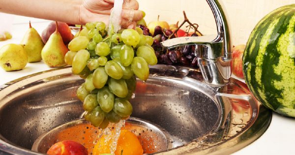 Woman's hands washing grapes and other fruits in colander in sink