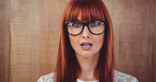 Surprised hipster woman posing face to the camera against wooden background